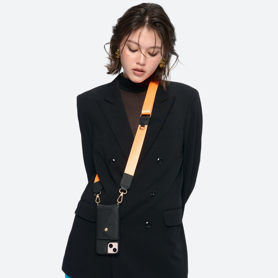 Model wearing the black Bandolier-style leather crossbody phone case, demonstrating its practicality with the adjustable strap comfortably slung over the shoulder.
