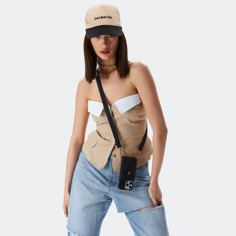 Model wearing the black Bandolier-style leather crossbody phone case, demonstrating its practicality with the adjustable strap comfortably slung over the shoulder.